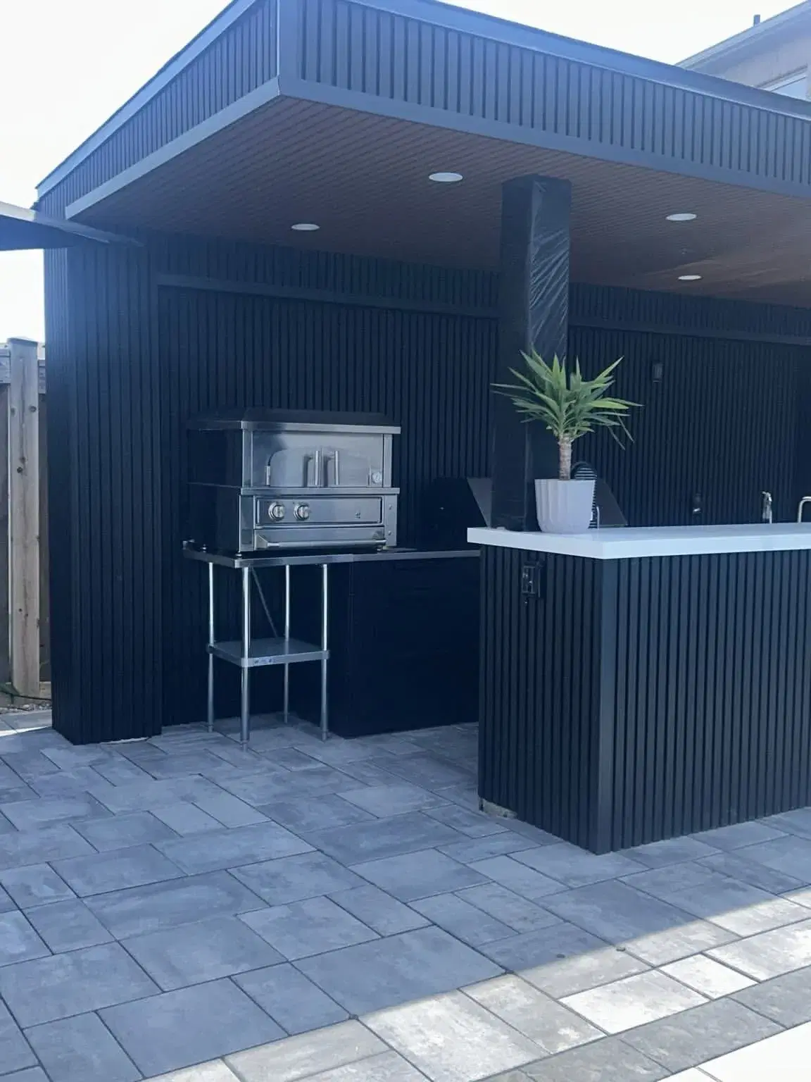 Modern black outdoor kitchen and bar with slat cladding on a paver patio