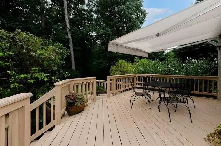 Composite deck with a retractable awning and railing overlooking a wooded backyard